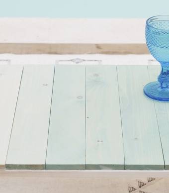 Mesa com ripas de madeira pintada em tons de azul em degradê com um copo por cima